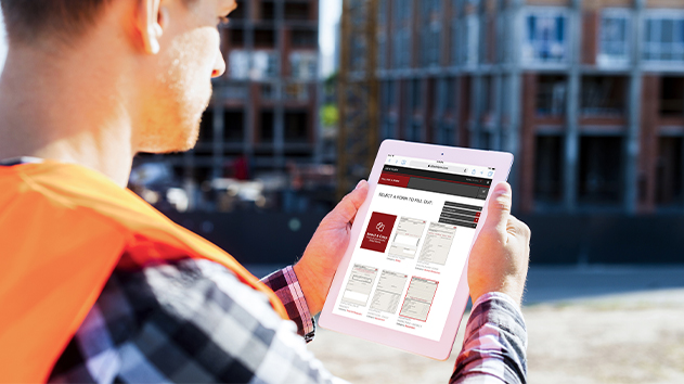 Construction worker in a safety vest using the Adobe Fill & Sign app on a tablet at a construction site with a building structure in the background.
