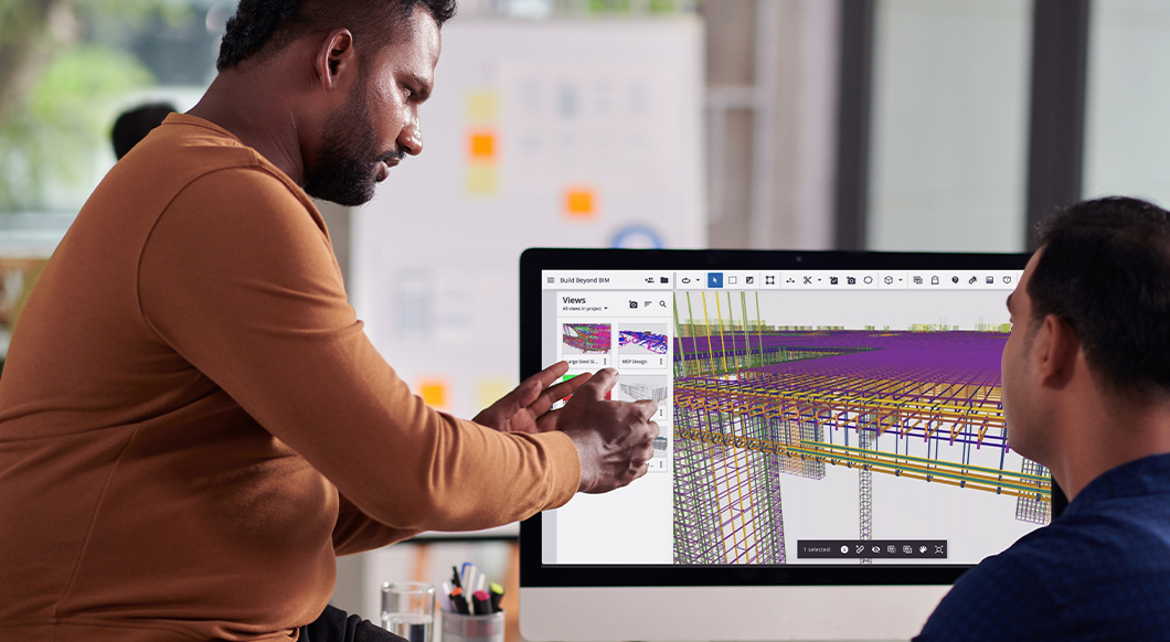 A man points at a computer screen displaying a 3D structural model in the Trimble "Build Beyond BIM" software interface as a colleague looks on.