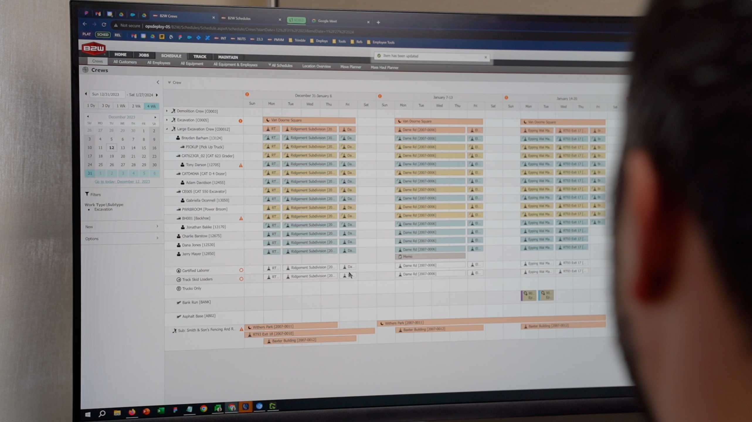 A person views the B2W Schedule interface by Trimble, showing construction crew and equipment assignments across multiple project sites.