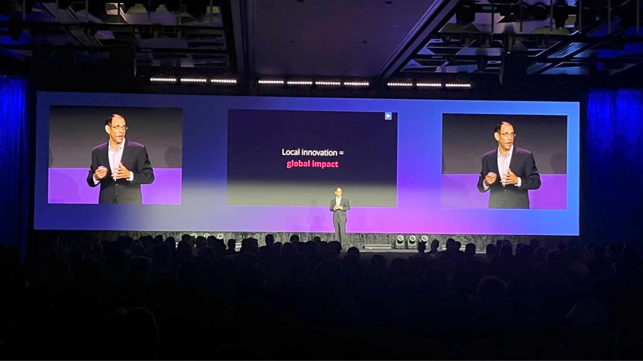 Trimble CEO Rob Painter presents at Trimble Dimensions. A slide reads "Local innovation = global impact" on a purple-lit stage.