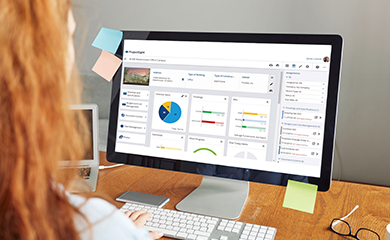 A person at a desk views a computer monitor displaying the Trimble ProjectSight project management software dashboard.
