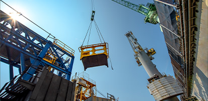 A crane lifts a yellow material bin at an industrial site, illustrating Trimble’s crane monitoring and lifting solutions.
