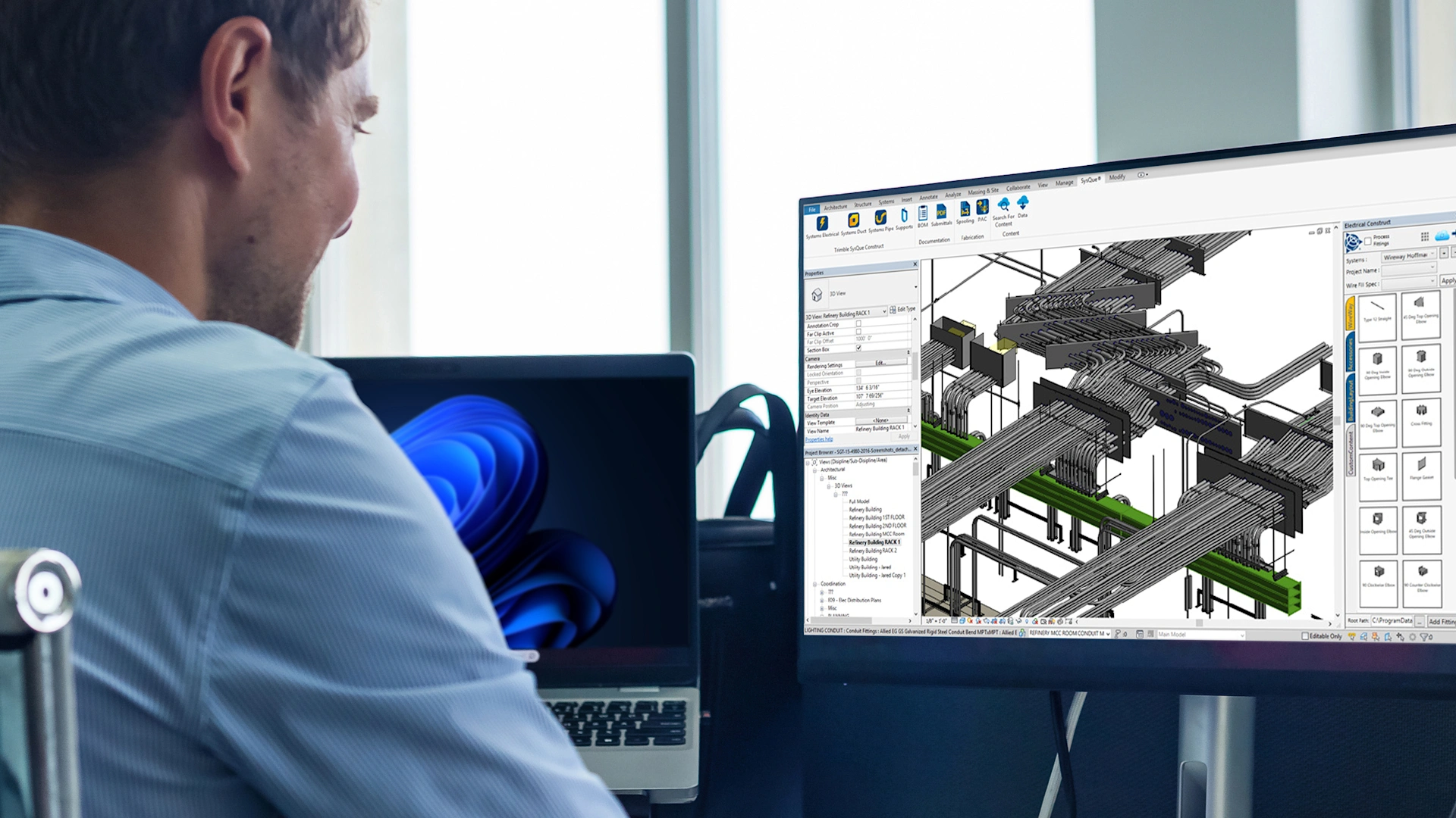 A man uses Trimble SysQue Construct software to design a 3D electrical conduit and MEP layout on a computer monitor.