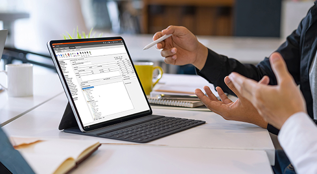 Two professionals collaborate over a tablet running Trimble construction management software in a modern office setting.