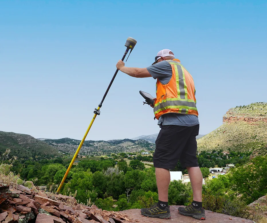 Man with reflective vest using Trimble Geospatial equipment on a plateau