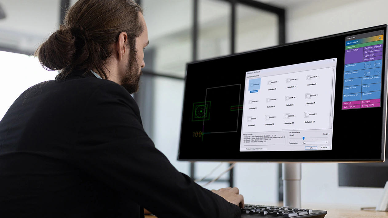 MEP engineer at desk viewing Stabicad for IntelliCAD on a monitor.