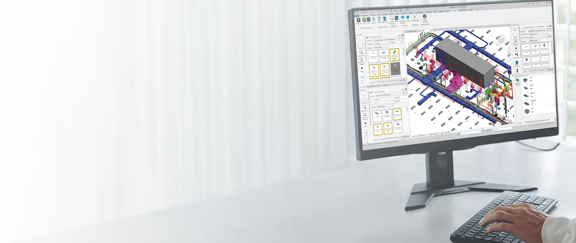 A person's hands are shown at a desk, typing on a keyboard while a monitor displays Trimble SysQue software.