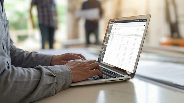 A person uses a laptop to access Trimble Spectrum construction management software in a professional setting.