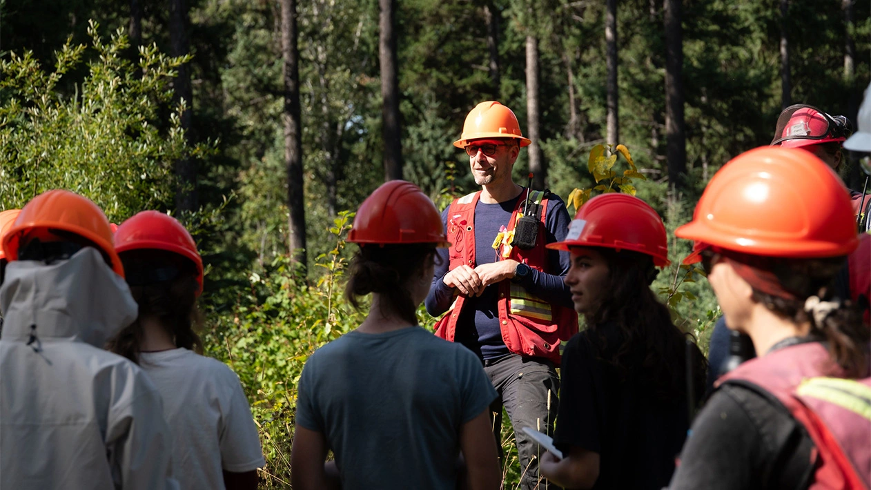 Professor guiding students wearing hard hats at research forest at University of British Columbia