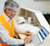 A construction professional in a safety vest uses a laptop displaying the Trimble Construction One dashboard. A hard hat and blueprints are nearby.