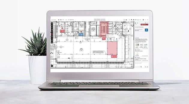 A laptop on a desk displays a digital floor plan with RFI markers in Trimble ProjectSight software, next to a small potted succulent.