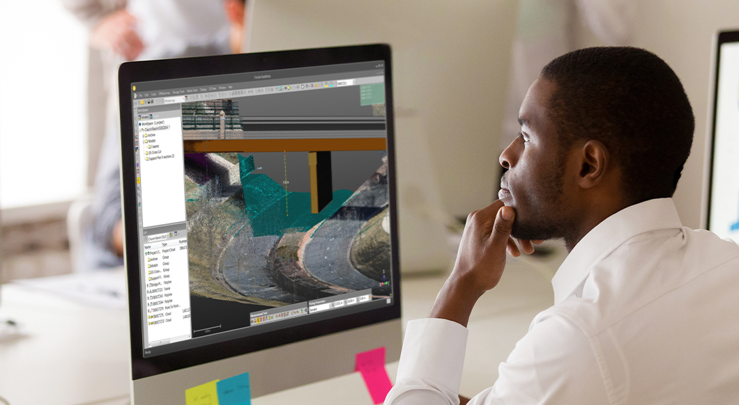 An engineer uses Trimble RealWorks software to analyze a 3D point cloud model of a bridge and road infrastructure project on a desktop monitor.