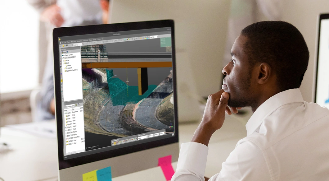An engineer uses Trimble RealWorks software to analyze a 3D point cloud model of a bridge and road infrastructure project on a desktop monitor.
