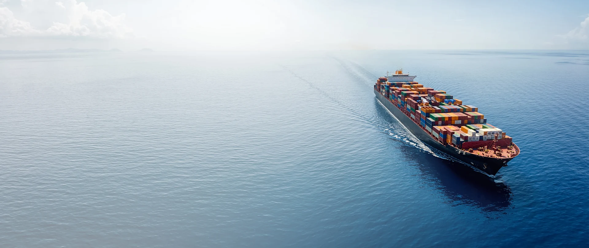 Aerial view of a container ship with colorful cargo sailing on a blue ocean, illustrating Trimble transportation and logistics services.