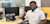 Young professional man at desk in front of computers smiling at camera giving a thumbs up