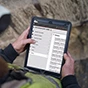 A construction worker in a safety vest uses Trimble Viewpoint Field View on a rugged tablet to manage project data at a job site.