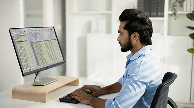 A person with a beard and dark hair sits at a desk, looking at a computer screen displaying Accubid Classic software.