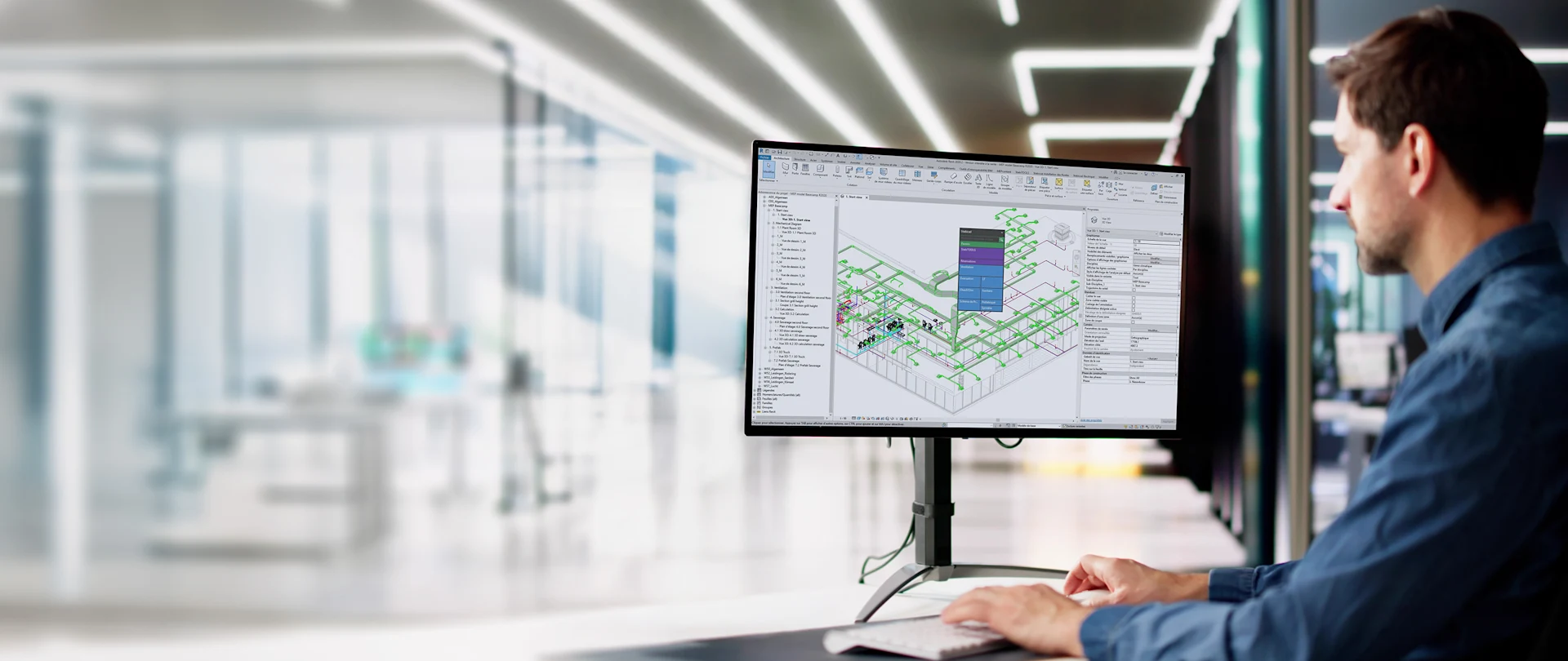 An engineer works in an office using Stabicad for Revit on a monitor to design complex MEP piping and ductwork systems in a detailed 3D BIM model.