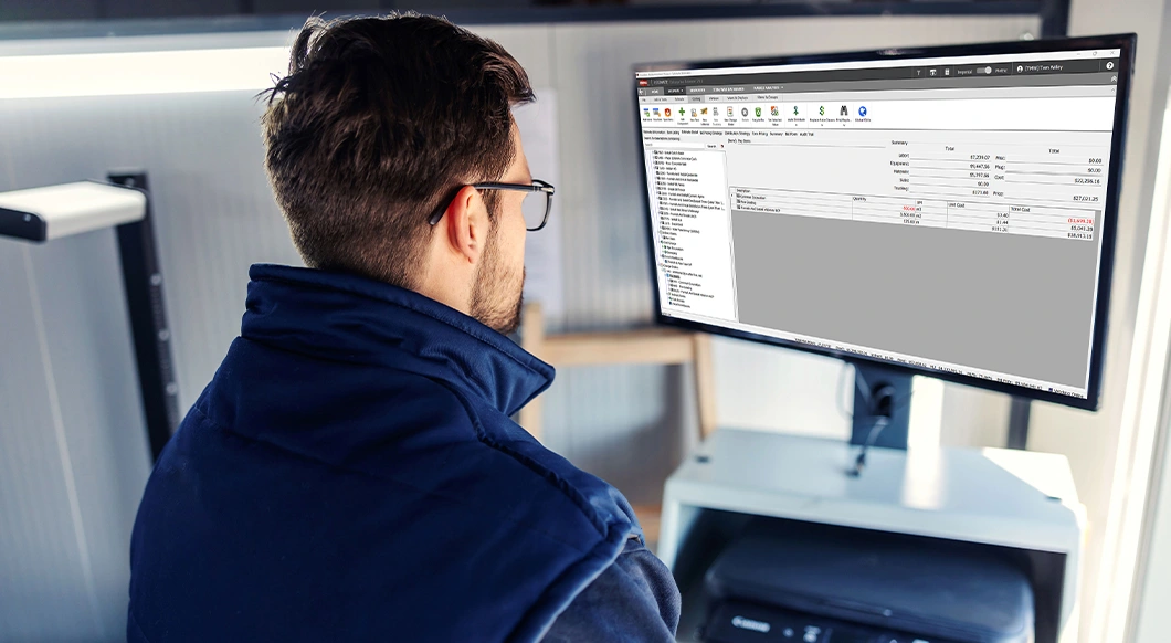 A man views HCSS HeavyBid construction estimating software, a solution distributed by Trimble, on a desktop computer monitor.
