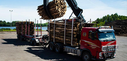 Ein mechanischer Kran auf einem Lagerplatz verlädt Baumstämme auf einen roten Lastwagen und veranschaulicht damit die Transport- und Logistiklösungen von Trimble Forestry.