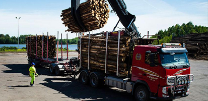 A mechanical crane loading logs onto a red truck at a timber yard, illustrating Trimble Forestry's wood transportation and logistics solutions.