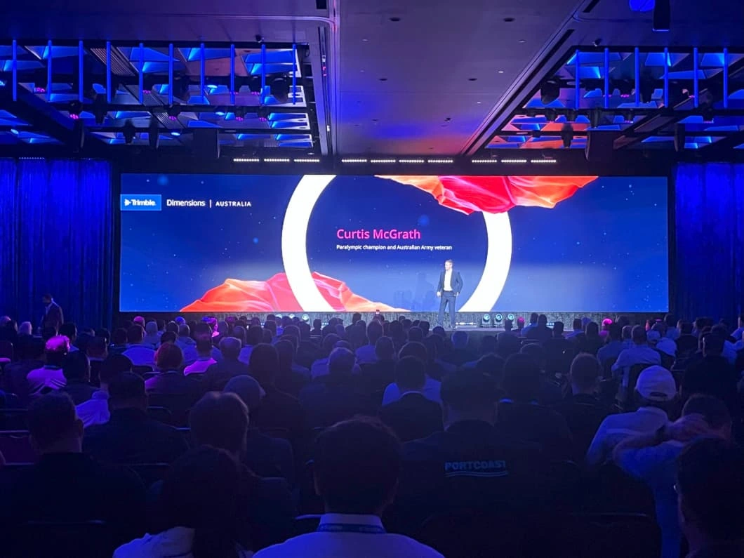 A keynote speaker on stage at the Trimble Dimensions Australia conference in Brisbane before a large seated audience.