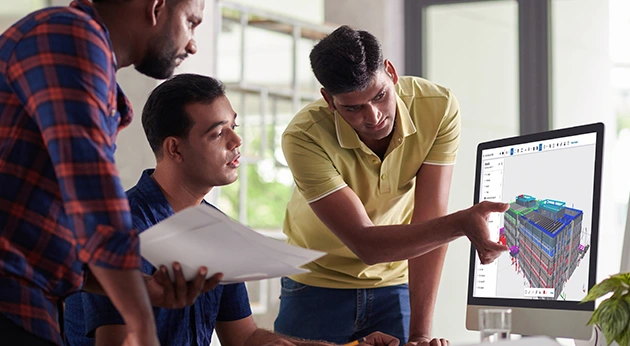 Three professionals review a 3D building model in Trimble Connect on a monitor while collaborating in an office.