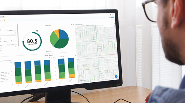 A man views a Trimble pavement management dashboard featuring a map and charts with an 80.5 Average PCI score for road assets.