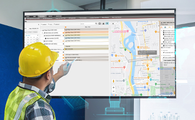 A generic worker in a yellow hard hat points to a monitor displaying Trimble's job planning software with a map and resource scheduling dashboard.