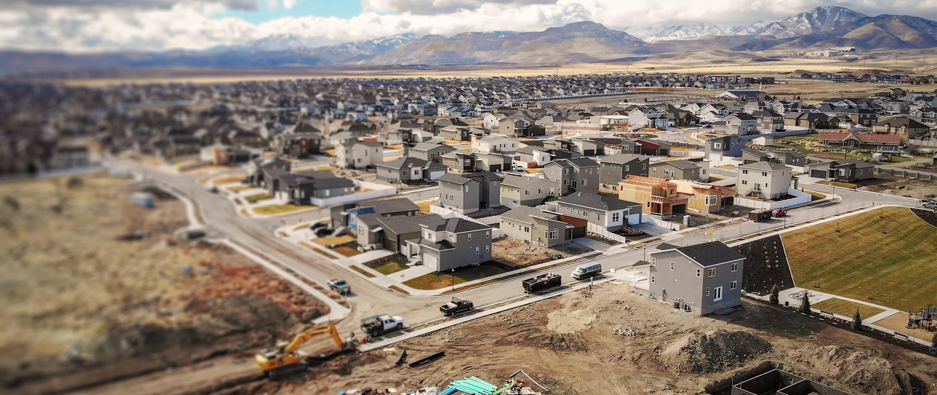 An aerial view shows a new housing development with construction happening in the foreground, and mountains in the background.