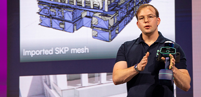 A presenter at the Dimensions Innovation Zone demonstrates a handheld scanning device in front of a screen showing an imported SKP mesh.