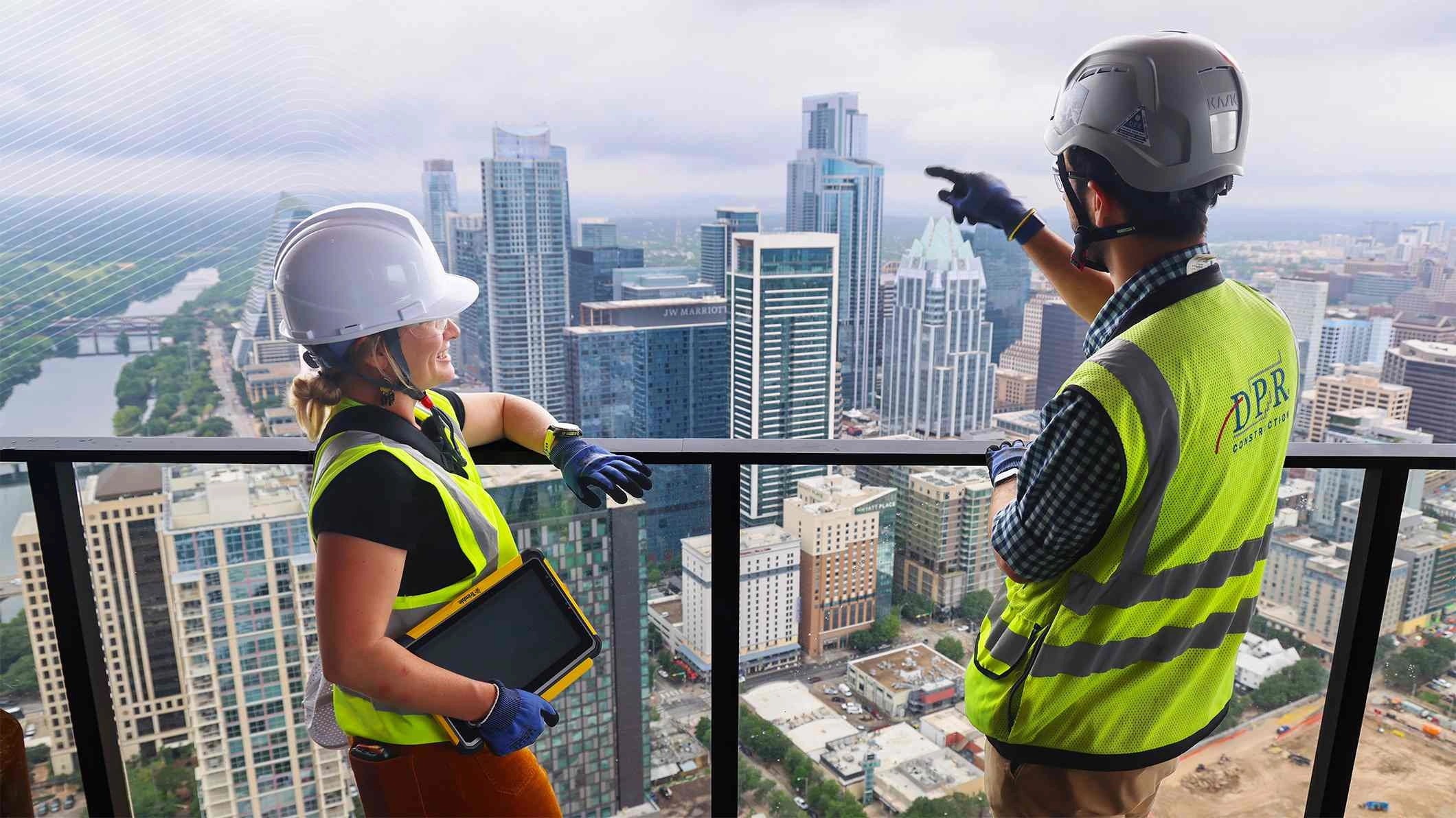 Deux personnes de DPR Construction regardent la ligne d'horizon d'Austin, au Texas, depuis le balcon d'un gratte-ciel. L'une d'elles tient une tablette renforcée Trimble jaune.