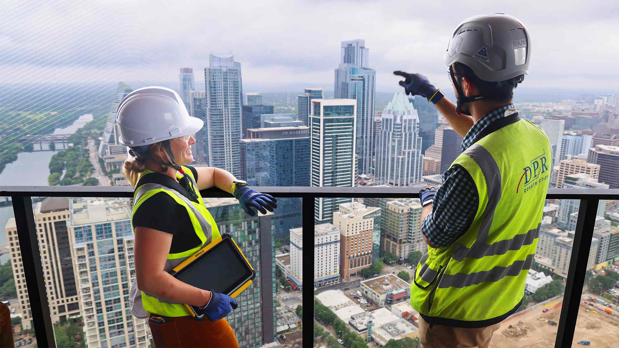 Two DPR construction workers overlook the Austin, Texas skyline from a high-rise balcony. One holds a yellow Trimble rugged tablet.