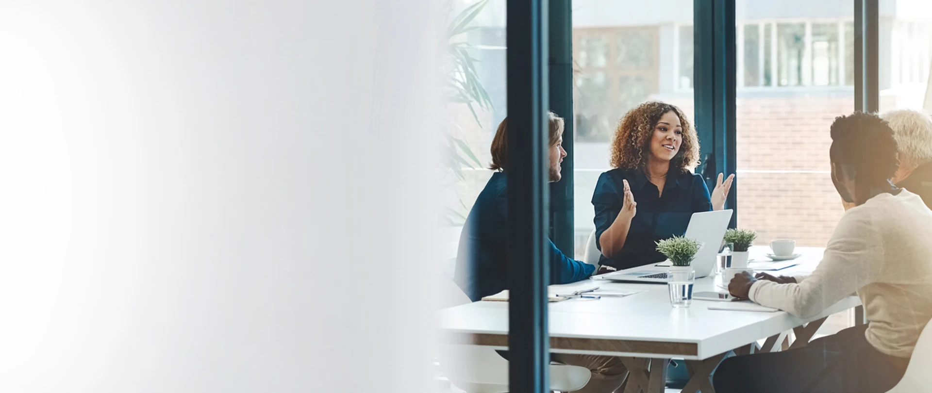 Diverse professionals collaborate in a bright office; a woman with curly hair gestures expressively during a meeting around a table.