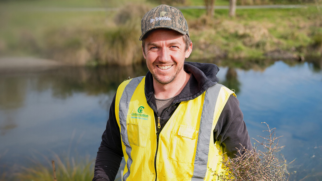 Trimble employee smiling at camera while holding a shovel to plant trees on service day