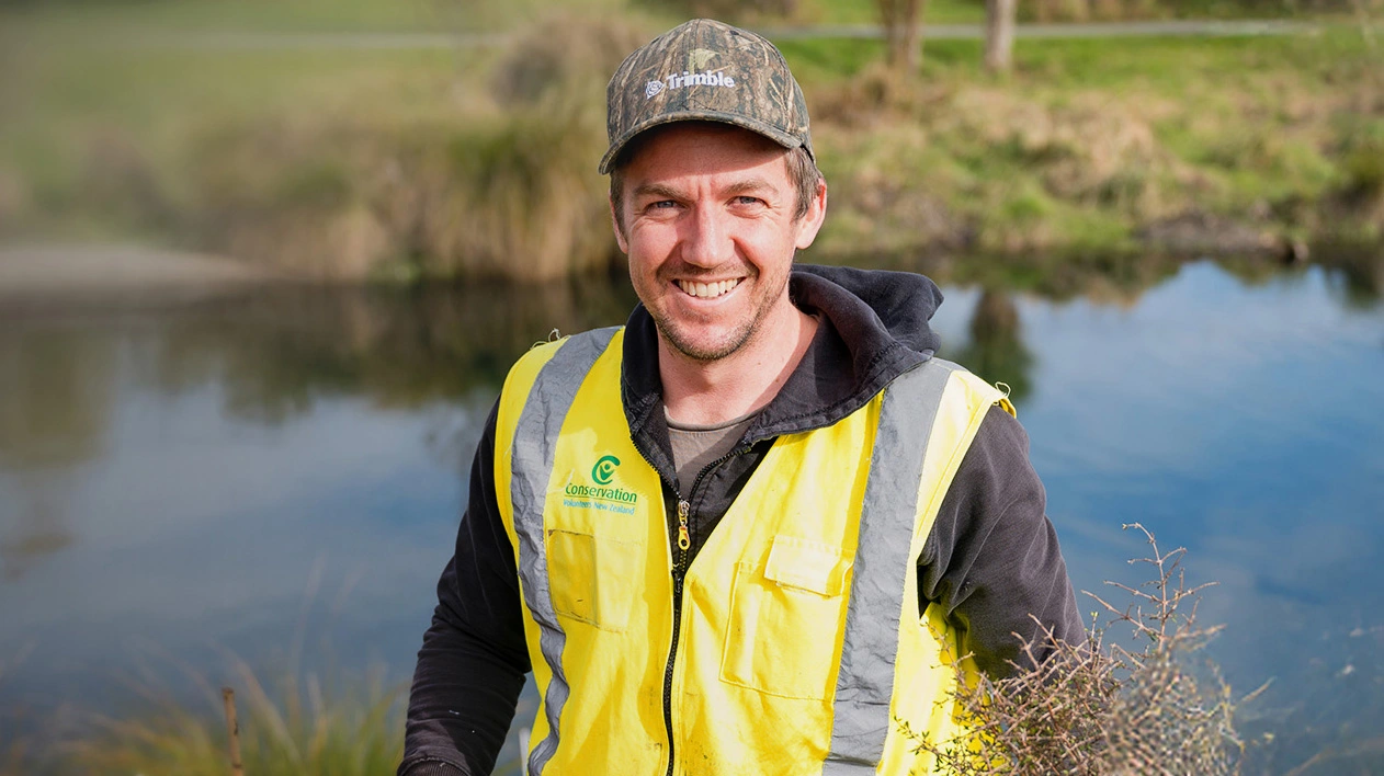 Trimble employee smiling at camera while holding a shovel to plant trees on service day