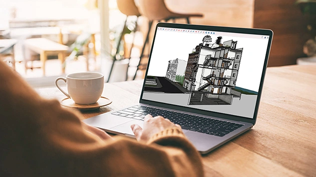 A person uses a laptop in a cafe to work on a 3D architectural cutaway model of a building in Trimble's SketchUp software.