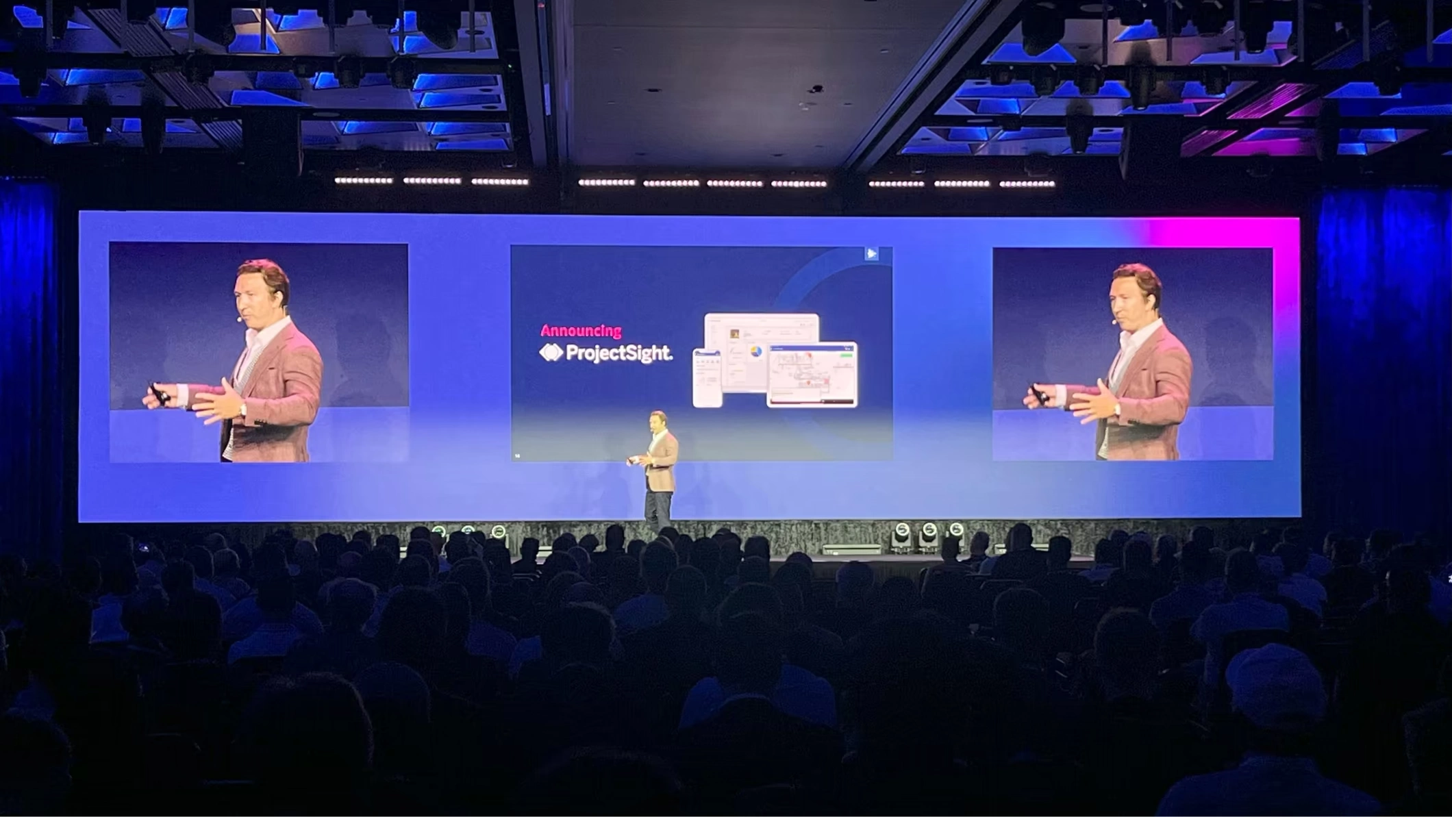 A speaker announces ProjectSight on stage at the Trimble Dimensions user conference in Las Vegas, with the announcement displayed on a large screen.