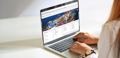 A person in a white shirt uses a laptop showing a colorful web page with cityscape graphics. The setting is bright and minimalistic.