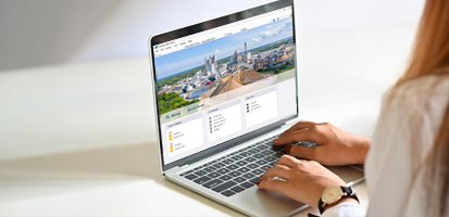 Iemand in een wit shirt gebruikt een laptop waarop een kleurrijke webpagina met stadsafbeeldingen wordt getoond. De setting is helder en minimalistisch.