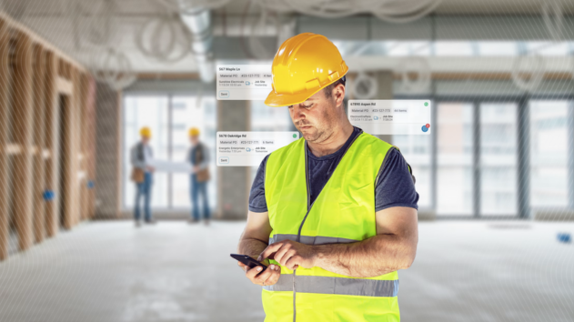 construction worker in the foreground wearing a yellow hard hat and a high-visibility safety vest looks down at his smartphone.