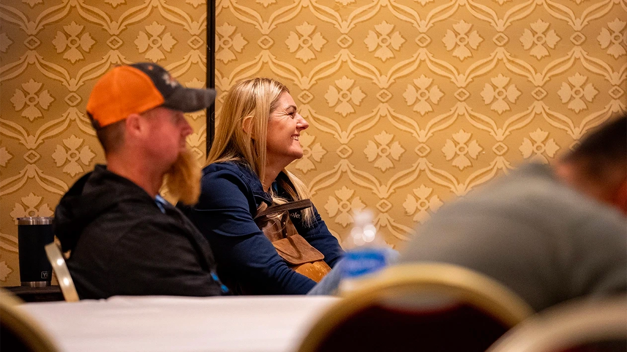 A Dimensions attendees smiles while watching a presentation in a session room.