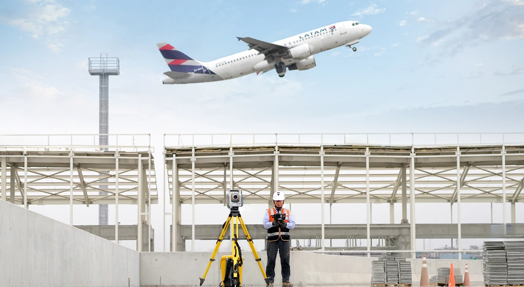 Construction person using Trimble Geospatial equipment at airport site with plane flying above