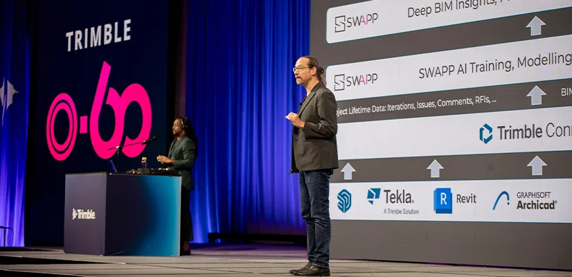 A presenter stands before a large digital screen detailing construction software workflows at the Trimble 0-60 Start-Up challenge.