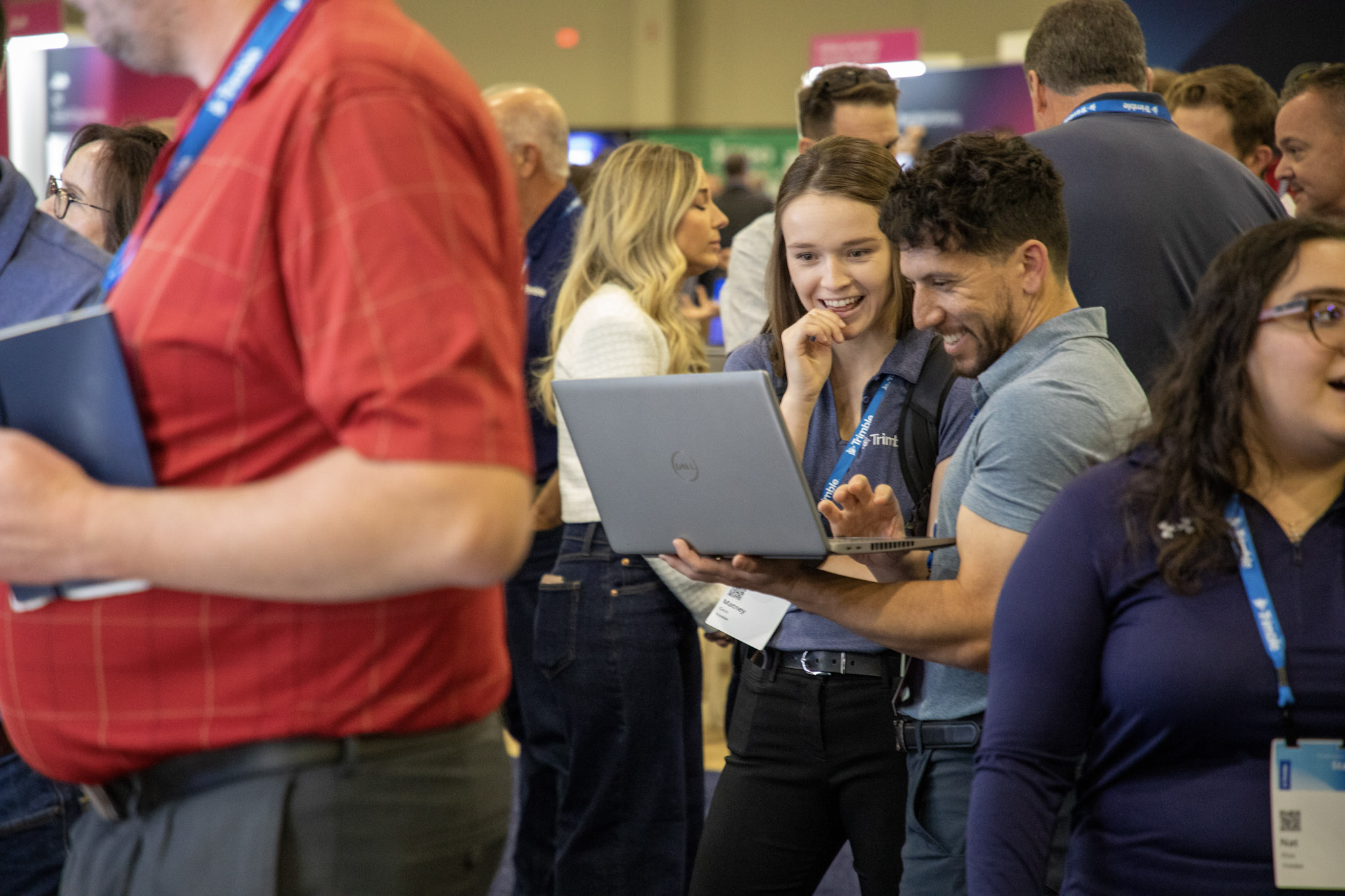 Trimble Dimensions attendees smile and laugh while looking at a laptop screen in the Expo Hall at The Venetian Resort.