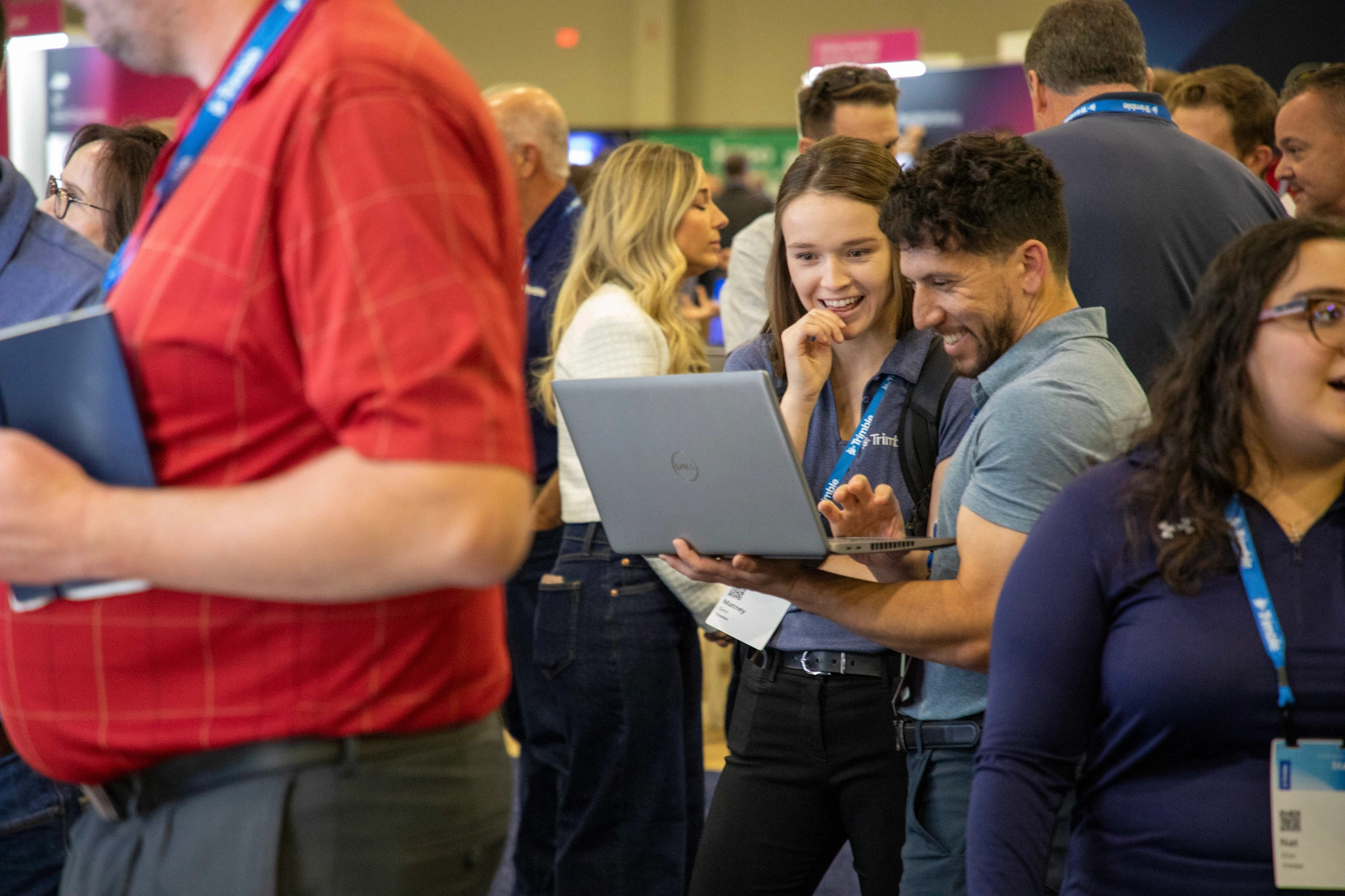 Trimble Dimensions attendees smile and laugh while looking at a laptop screen in the Expo Hall at The Venetian Resort.