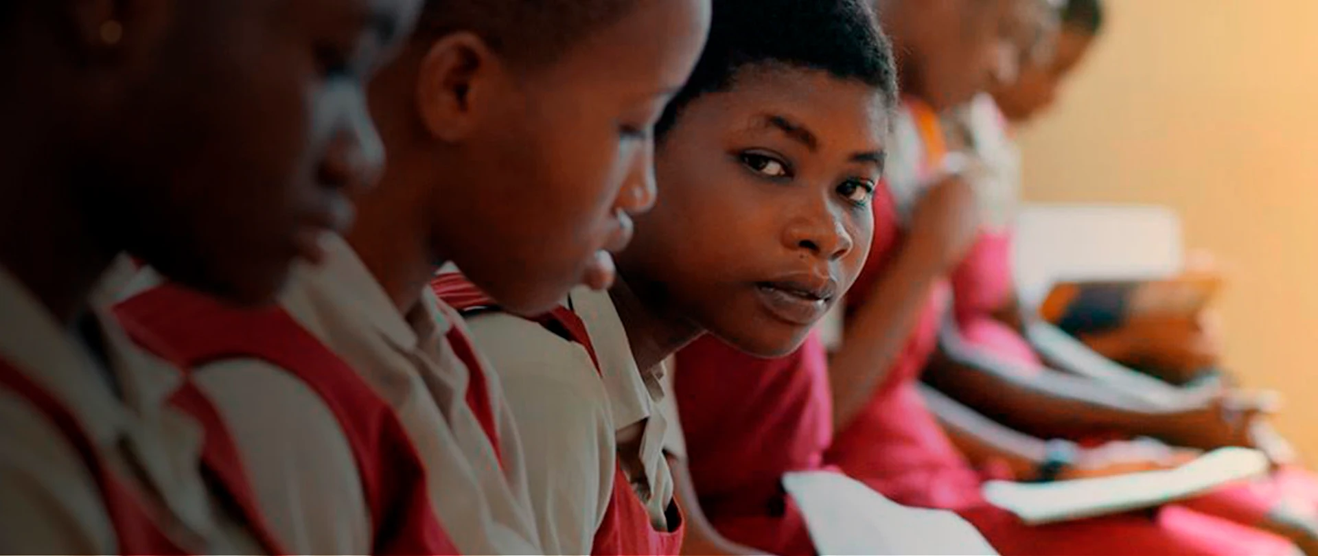 Female students wearing red sitting in classroom while holding papers