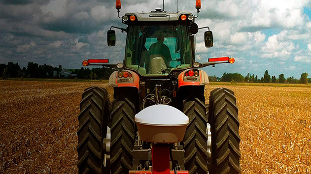 A rear-view, low-angle shot captures a modern tractor in a field of harvested crops under a dramatic, cloudy sky.
