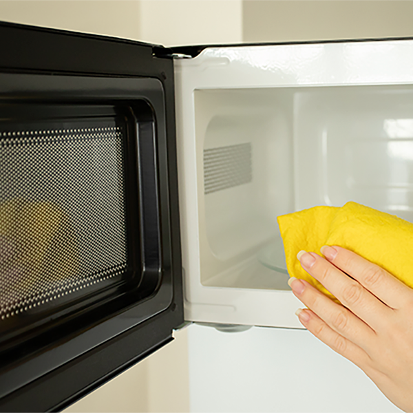 Hand holding a yellow cleaning cloth wiping the inside of an open microwave.