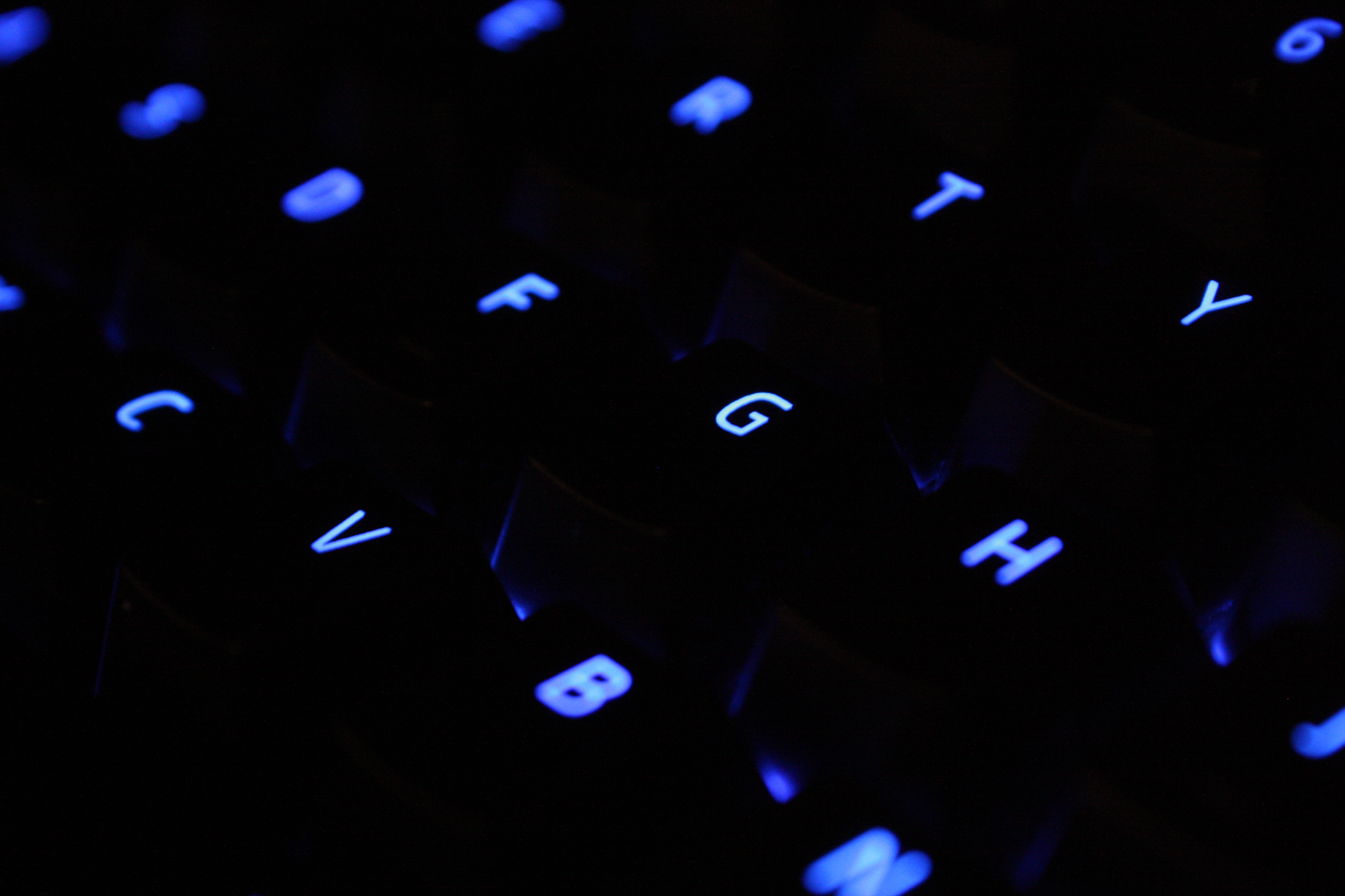 Black keyboard with blue glowing keys in the dark